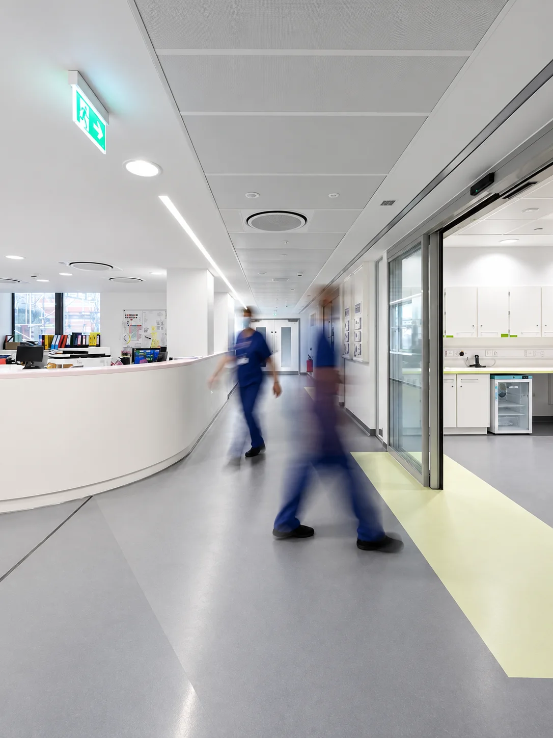 Hospital ward corridor with staff walking past the nurses’ station.